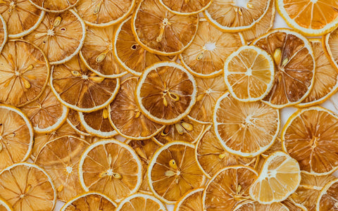 En bunke tørrede citroner i tynde skiver arrangeret i et cirkulært mønster på en træplade med krukker med mere tørret citrus i baggrunden.