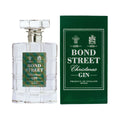 En klar Bond Street Gin-flaske med julegin i et firkantet mønster står ved siden af den matchende grønne æske med hvid tekst og festlige dekorationer.