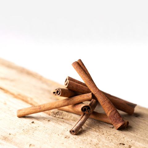Kanelstænger fra Frugtskiver.dk er arrangeret i en lille bunke på en lys træoverflade mod en almindelig hvid baggrund.
