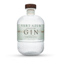 En klar 70 cl flaske Vert Azur Gin fra Vert Azur med en træhætte, ribbet nedre halvdel og en etiket med teksten "Olive - Fennel - Citrus". Ginen har en alkoholprocent på 43,8.