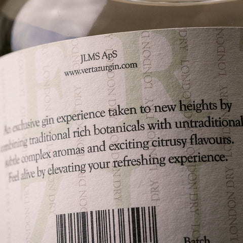 Et nærbillede af en Vert Azur Gin-flaskeetiket viser tekst om Vert Azurs unikke botaniske ingredienser, citrusnoter, hjemmeside og stregkode, der lover en forfriskende, ophøjet ginoplevelse.